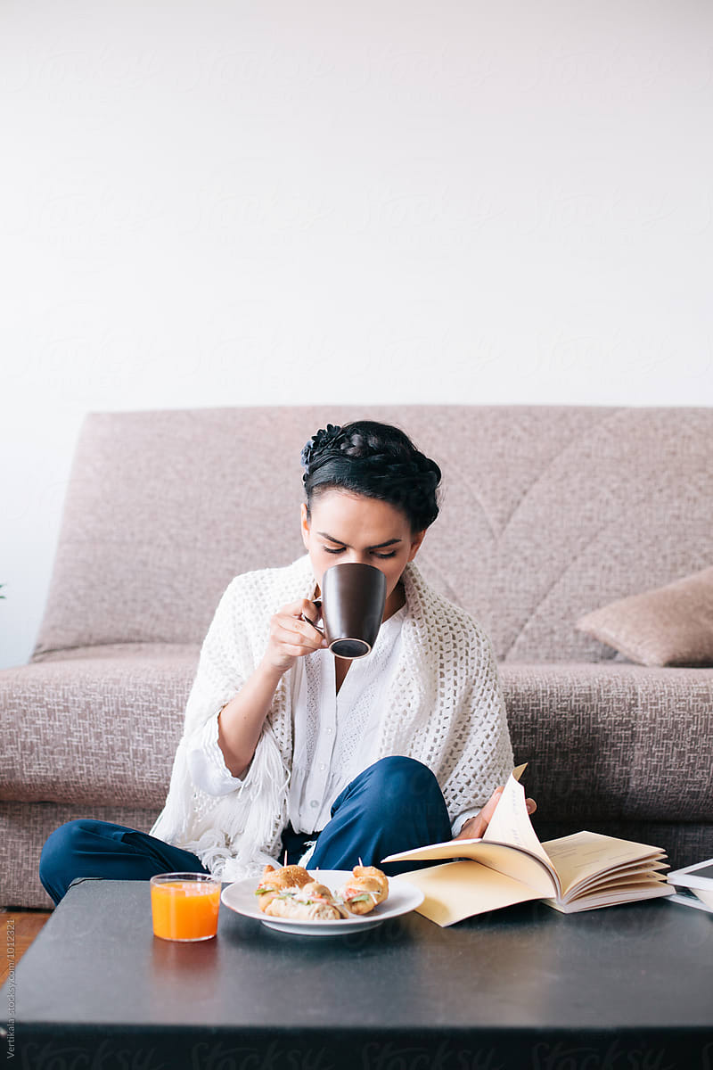 Stylish woman drinking coffee, having a breakfast and reading a book indoor