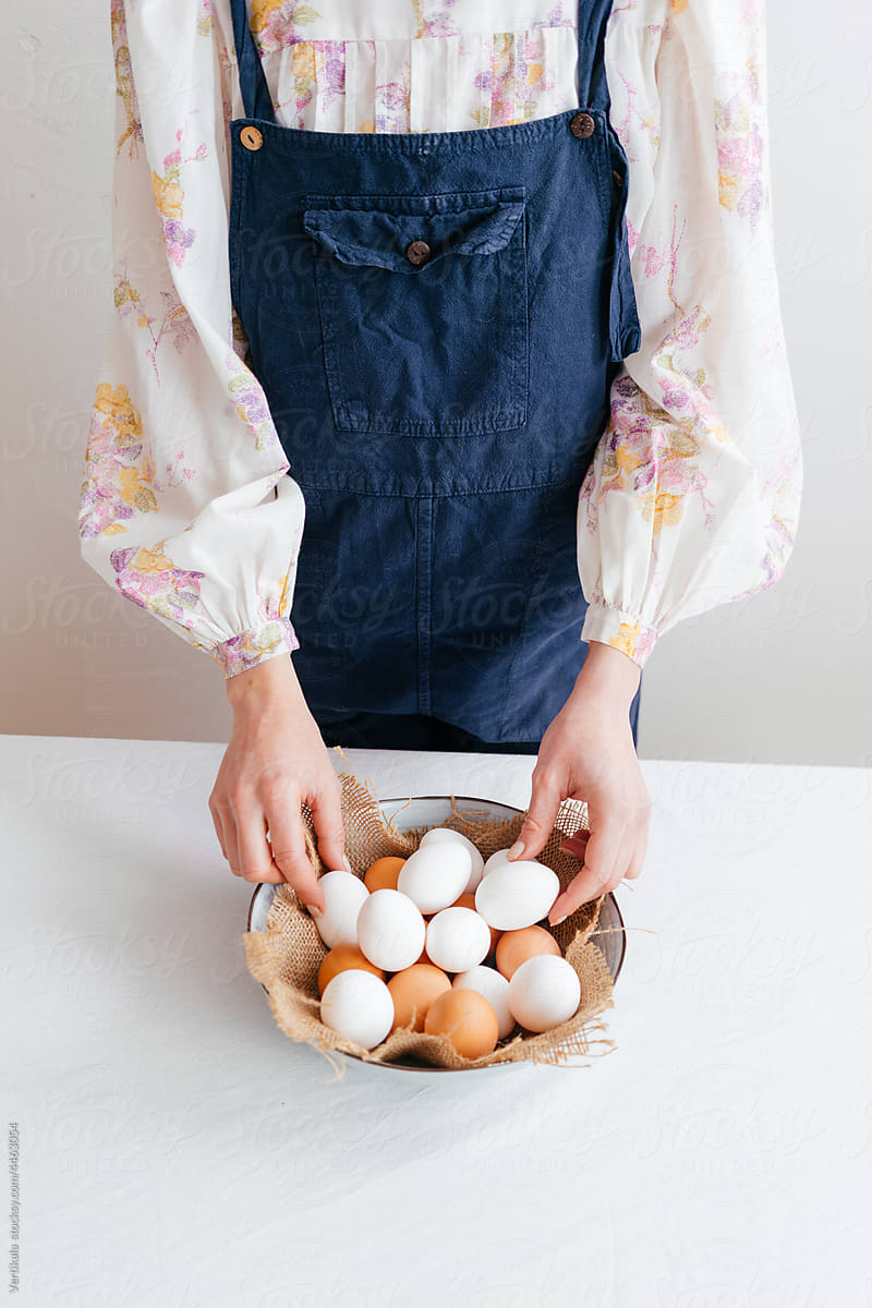 The anonymous woman arranges eggs in a bowl set on a linen table cloth.